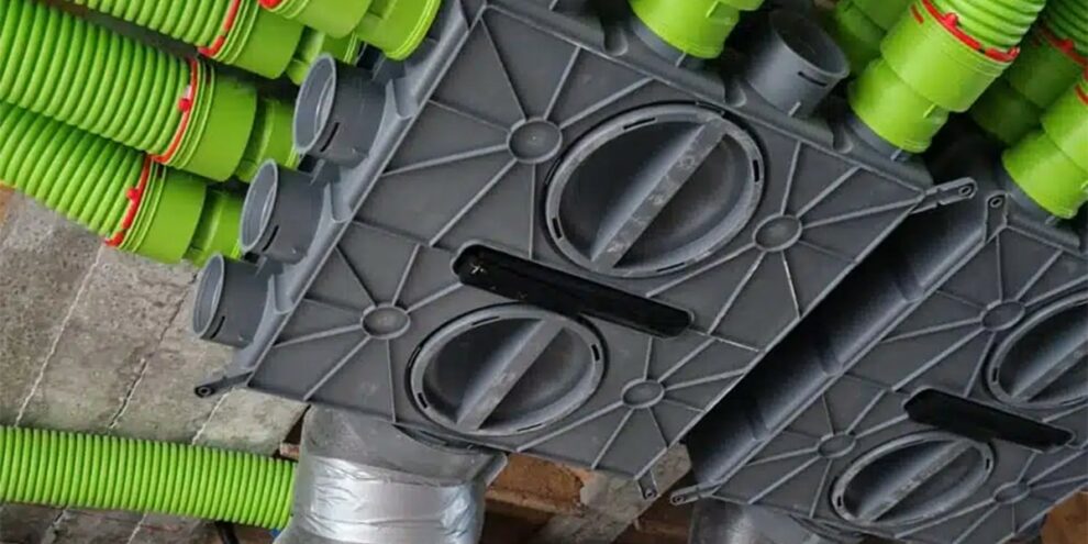 Caisson de distribution VMC avec gaines vertes raccordées, installé sur un mur en béton dans un réseau de ventilation domestique.