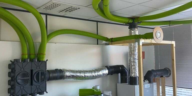 Système de ventilation mécanique contrôlée installé dans un laboratoire technique, montrant des gaines, un caisson de distribution et un module de VMC, illustrant les équipements concernés par les aides financières pour l’installation d’une VMC.