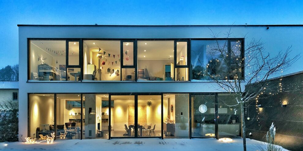Maison contemporaine à deux étages, éclairée de l’intérieur par plusieurs points lumineux, illustrant une installation électrique conforme à la norme NF C 15‑100.