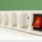 Gros plan sur une multiprise blanche avec interrupteur rouge lumineux, illustrant les limites de puissance et les risques de surcharge électrique.