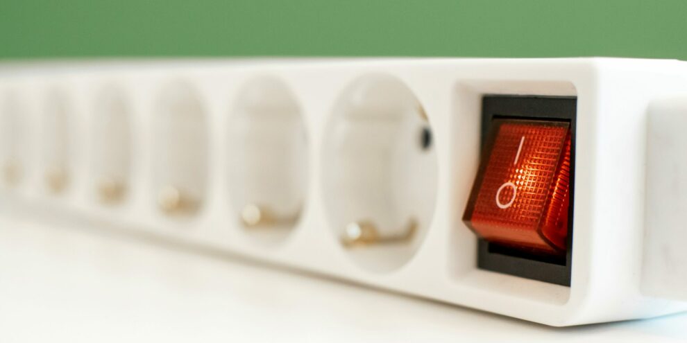 Gros plan sur une multiprise blanche avec interrupteur rouge lumineux, illustrant les limites de puissance et les risques de surcharge électrique.