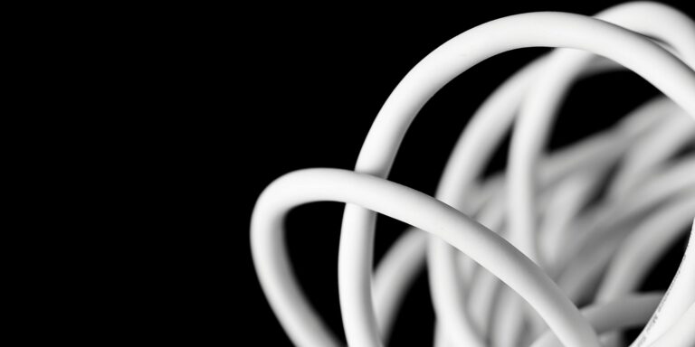 Rallonge électrique enroulée – effet Joule et dissipation thermique Gros plan artistique sur une rallonge électrique blanche enroulée, illustrant le phénomène de surchauffe par effet Joule lorsque le câble reste enroulé, sur fond noir minimaliste.
