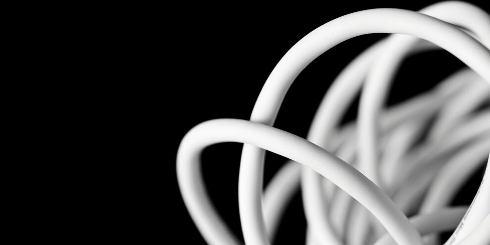 Gros plan artistique sur une rallonge électrique blanche enroulée, illustrant le phénomène de surchauffe par effet Joule lorsque le câble reste enroulé, sur fond noir minimaliste.